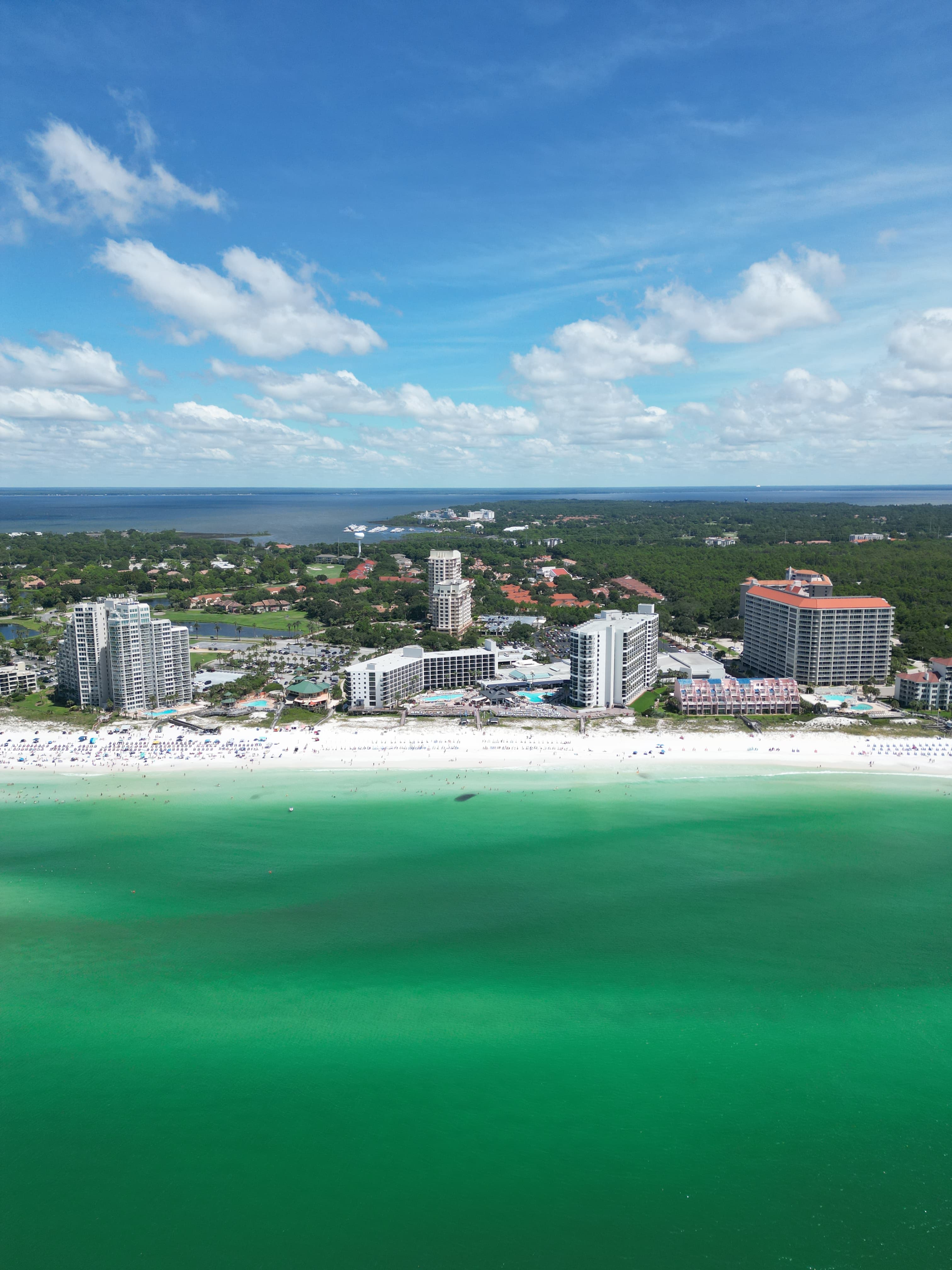 Aerial drone photo of Destin Florida beach with emerald green Gulf water, white sand, and resort hotels along shoreline